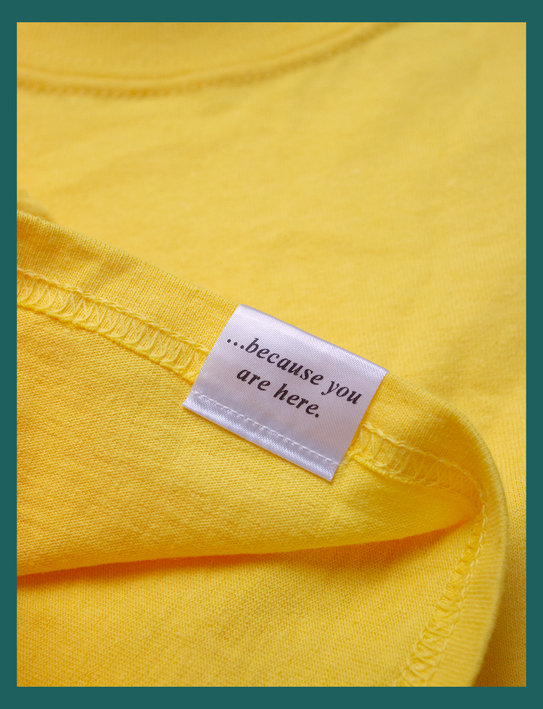 View of the underside of the appliqué label attached at the right cuff on the GOOD DAY Tee by KULT Clothing | It reads "...because you are here." in an italicised font | HD printed premium heavyweight satin label
