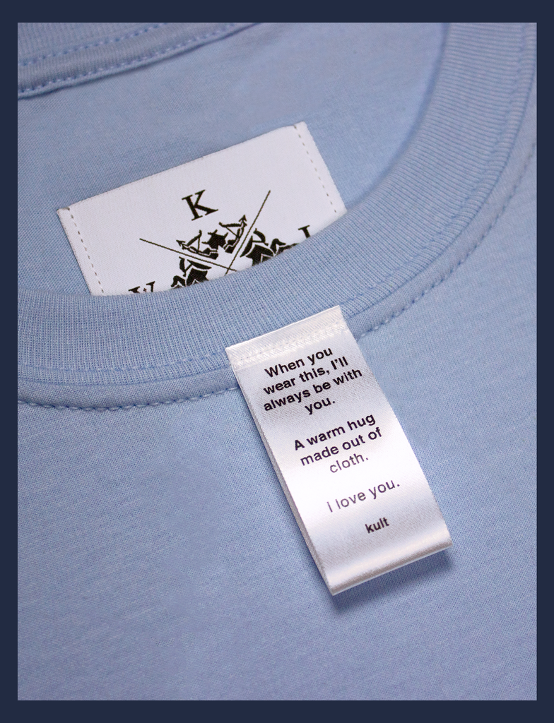 Close-up on the label of A WARM HUG Tee in Light Blue by KULT Clothing | When you wear this, I'll always be with you. A warm hug made out of cloth. I love you. KULT
