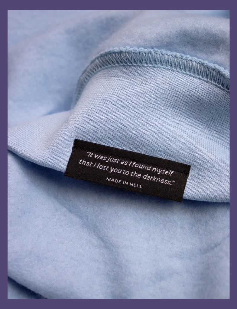 Close-up shot of the underside hem tag on the A WARM HUG Sweater in Light Blue by KULT Clothing | "It was just as I found myself that I lost you to the darkness." MADE IN HELL