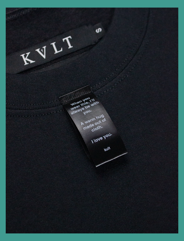 Close-up on the label of A WARM HUG Sweater in Black by KULT Clothing | When you wear this, I'll always be with you. A warm hug made out of cloth. I love you. KULT