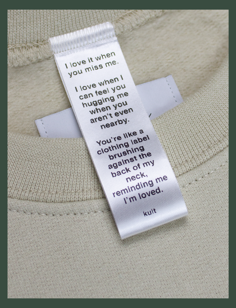 Close-up on the label of the DISTANT LOVE Sweater in Sandstone by KULT Clothing | I love it when you miss me.  I love when I can feel you hugging me when you aren’t even nearby.  You’re like a clothing label brushing against the back of my neck, reminding me I’m loved. KULT
