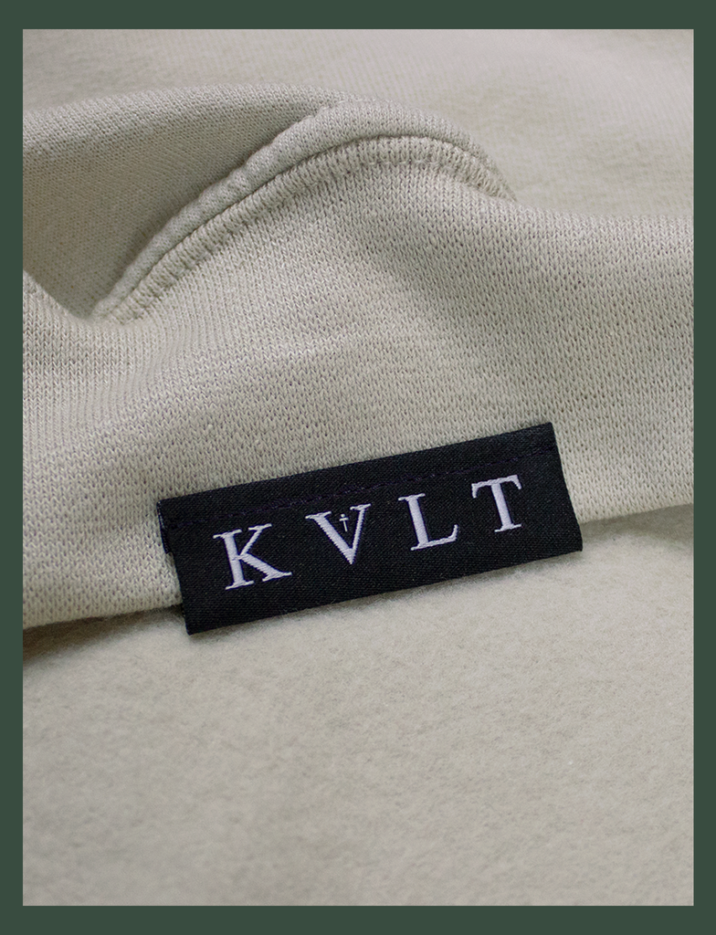 Close-up shot of the topside hem tag on the DISTANT LOVE Sweater in Sandstone by KULT Clothing | I love it when you miss me. I love when I can feel you hugging me when you aren’t even nearby. You’re like a clothing label brushing against the back of my neck, reminding me I’m loved. KULT | KVLT