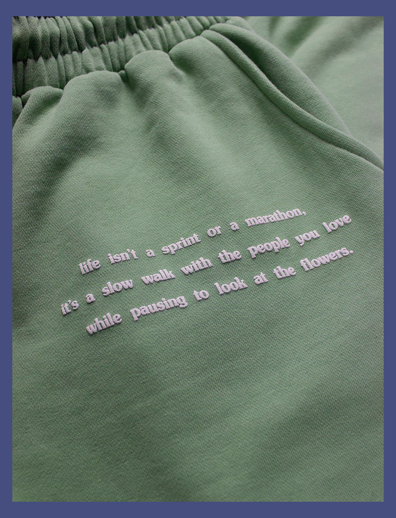 Close-up view of the hand-printed puff design at the front pocket on the EMBRACE Sweatpants in Sage by KULT Clothing | It reads "Life isn't a sprint or a marathon, it's a slow walk with the people you love while pausing to look at the flowers" | Hand-printed using eco friendly inks