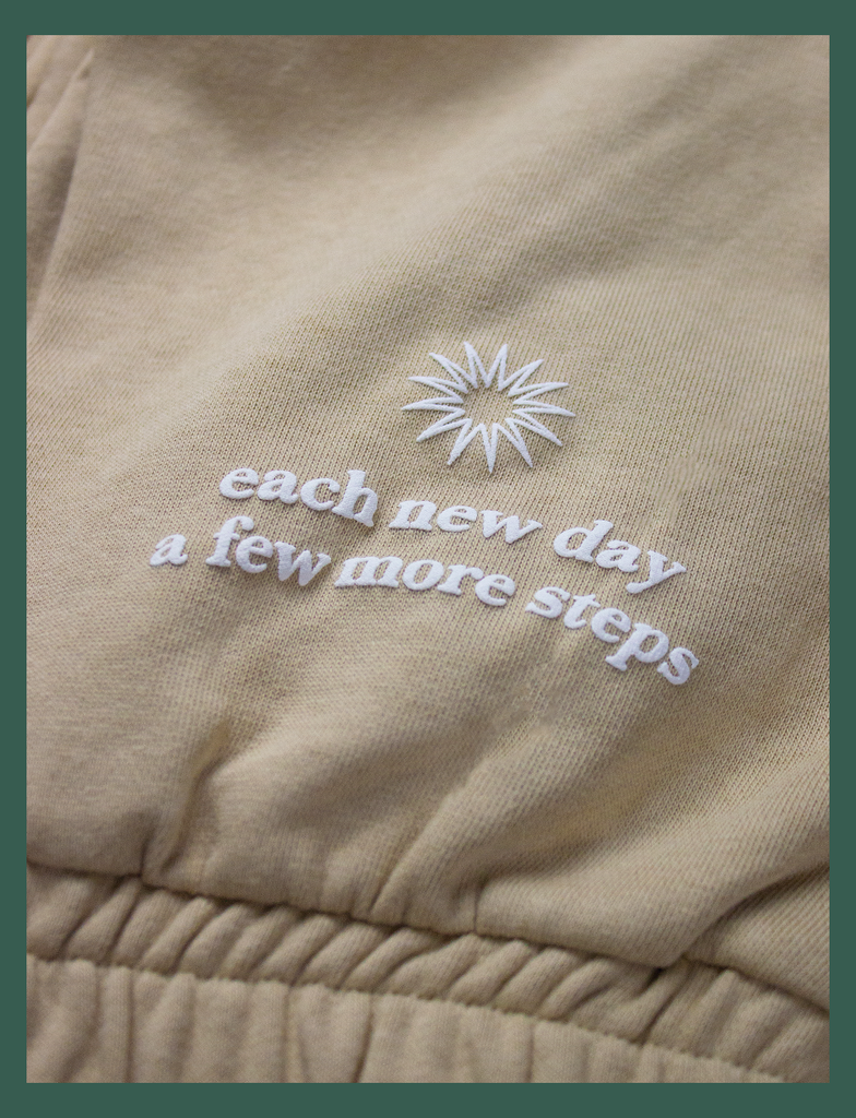 Close-up view of the hand-printed puff design on the EMBRACE Sweatpants in Rodeo by KULT Clothing | It reads "Each new day / A few more steps" next to a stylised illustration of a sunrise | Hand-printed using eco friendly inks