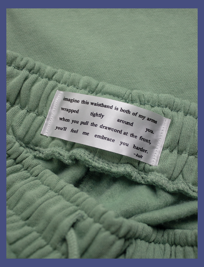 Detailed view of the premium heavyweight satin label stitched to the inside of the waistband on the EMBRACE Sweatpants in Sage by KULT Clothing | It reads "Imagine this waistband is both of my arms wrapped tightly around you. When you pull the drawcord at the front, you'll feel me embrace you harder. ~kult" | HD printed label made from premium heavyweight satin with anti-fray technology