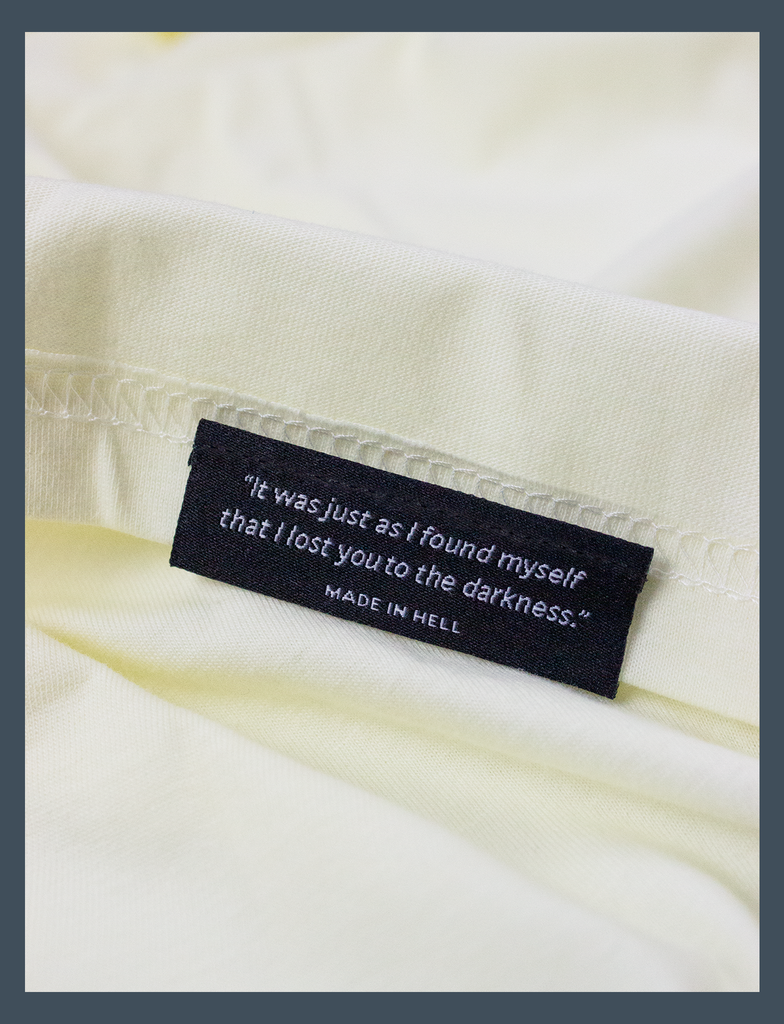 Close-up view of the underside hem tag detailing on the SADIFORNIA Tee in Primrose by KULT Clothing | eco-friendly, climate neutral t-shirt | "It was just as I found myself that I lost you to the darkness." MADE IN HELL