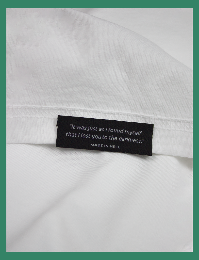 Close-up of the underside hem label on THE CALL Tee in White by KULT Clothing | eco-friendly, climate neutral t-shirt | "It was just as I found myself that I lost you to the darkness." Made in Hell