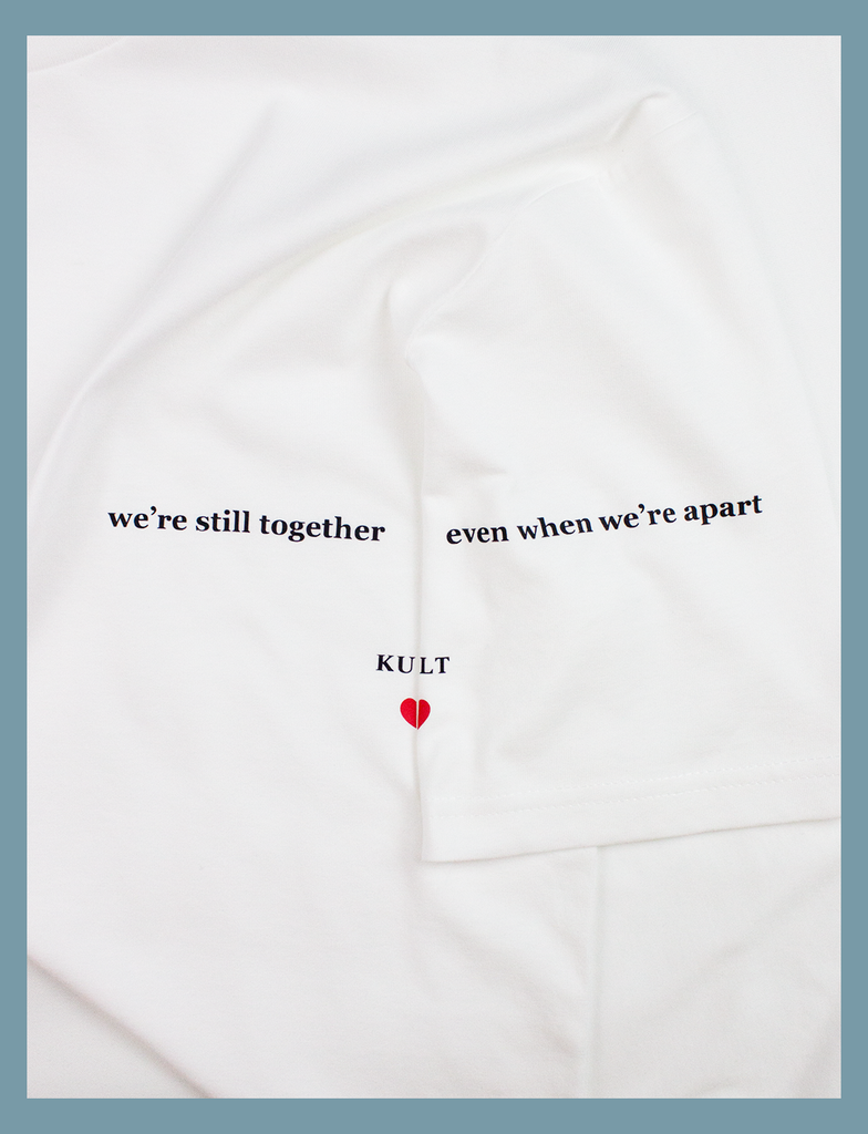A full close-up view of the design on the ALWAYS TOGETHER Tee in White by KULT Clothing | It reads "We're still together even when we're apart" printed across the left breast and sleeve using our matte black and red Barely There™ vinyl | eco-friendly, climate neutral t-shirt