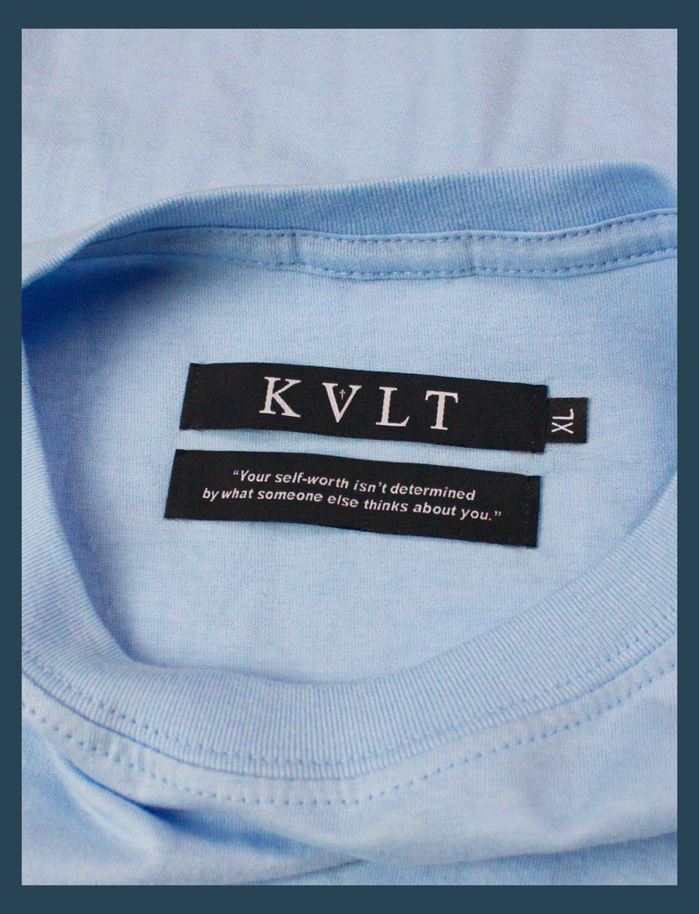 A close-up shot of the twin neck labels on the LOVED Tee in Light Blue by KULT Clothing | The bottom label reads "Your self-worth isn't determined by what someone else thinks about you." | KULT