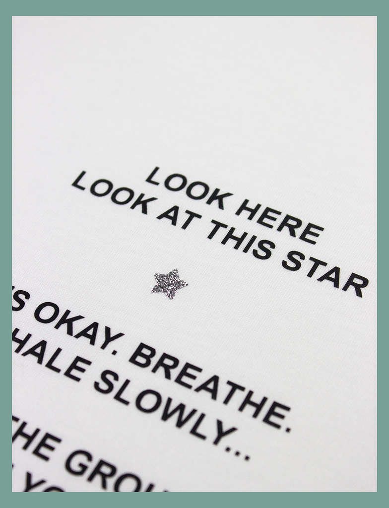 Close-up view of the glittery star and print on the PAUSE Tee in White by KULT Clothing | It reads "Look here. Look at this star." with a silver, glittery star just below | Printed using our matte black and silver glitter Barely There™ vinyl