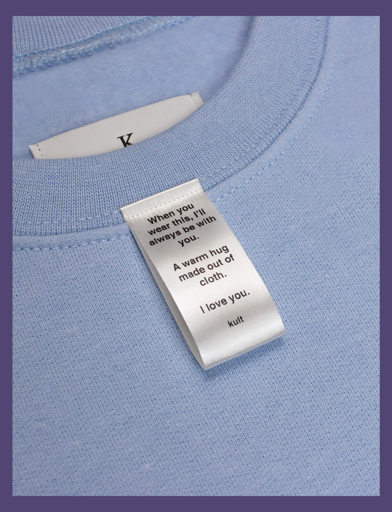 Close-up on the label of A WARM HUG Sweater in Light Blue by KULT Clothing | When you wear this, I'll always be with you. A warm hug made out of cloth. I love you. KULT