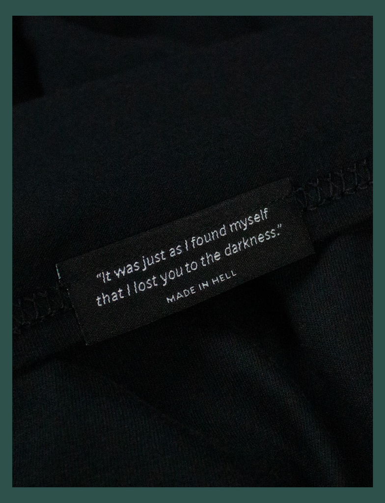 Close-up on the underside of the bottom seam label of A WARM HUG Tee in Black by KULT Clothing | "It was just as I found myself that I lost you to the darkness." Made in Hell.