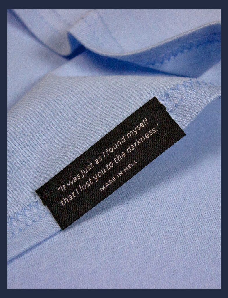 Close-up on the underside of the bottom seam label of A WARM HUG Tee in Light Blue by KULT Clothing | "It was just as I found myself that I lost you to the darkness." Made in Hell.