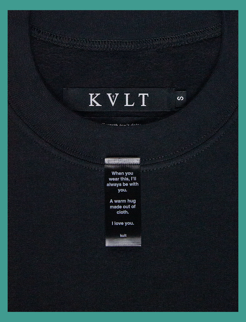 Another close-up on the label on the front neckline of A WARM HUG Sweater in Black by KULT Clothing | When you wear this, I'll always be with you. A warm hug made out of cloth. I love you. KULT