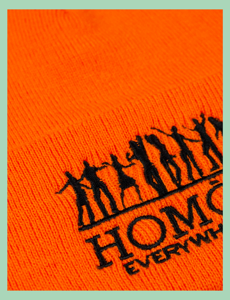 Close-up of the design on the HOMOS Beanie by KULT Clothing | "Homos Everywhere" embroidered design on an orange beanie hat