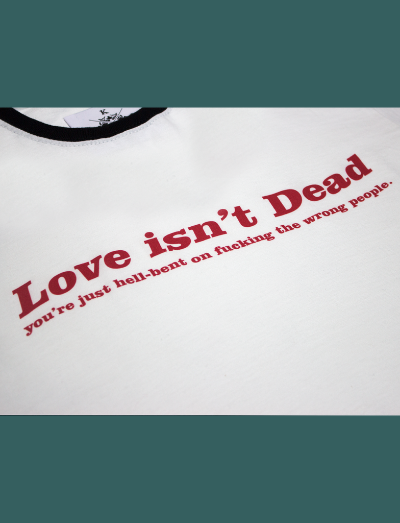Close-up view of the LOVE ISN'T DEAD Tee in a White Ringer style by KULT Clothing | eco-friendly, climate neutral t-shirt | Love isn't Dead you're just hell-bent on fucking the wrong people.