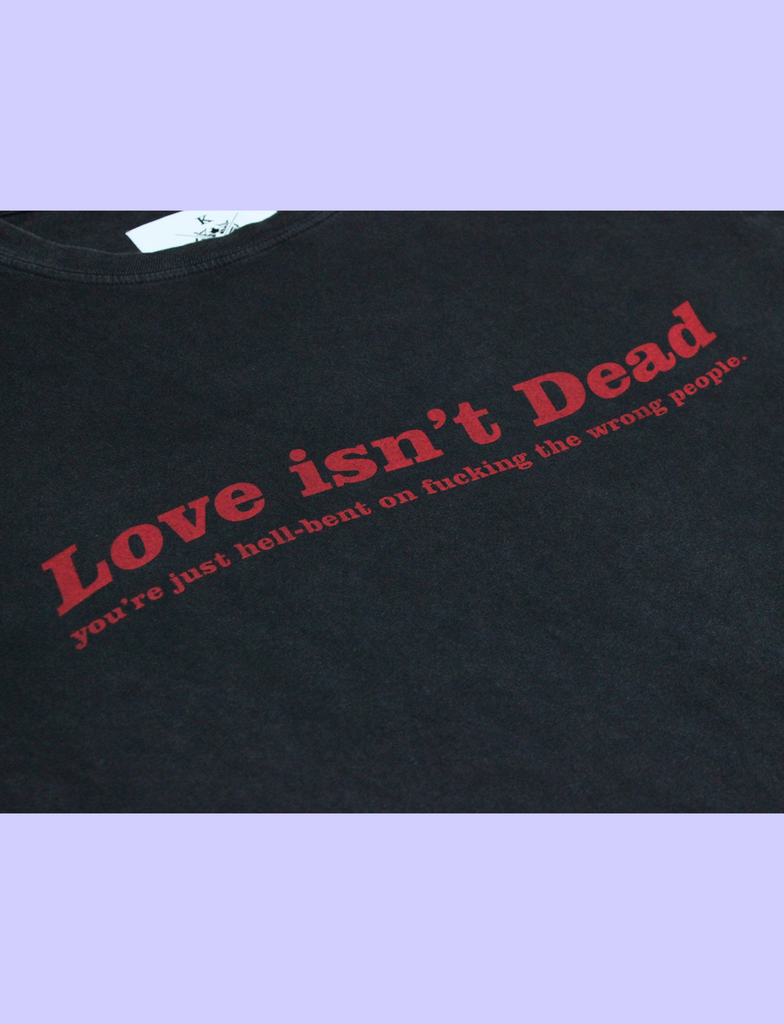 Close-up of the LOVE ISN'T DEAD Tee in Sun-Bleached Black by KULT Clothing | eco-friendly, climate neutral t-shirt | Love isn't Dead you're just hell-bent on fucking the wrong people.