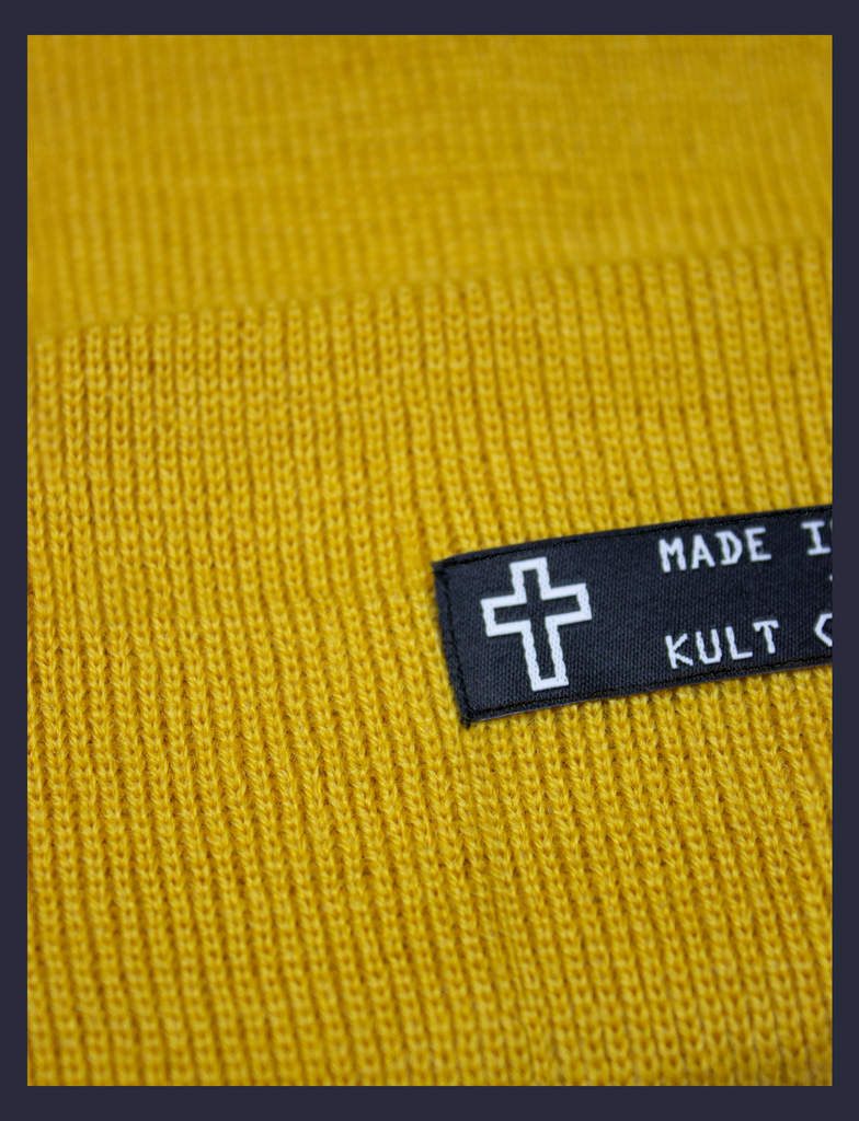 Close-up detail on the MADE IN HELL Beanie in Mustard by KULT Clothing | Black appliqué label on the front of a mustard-coloured, 100% acrylic knit beanie hat
