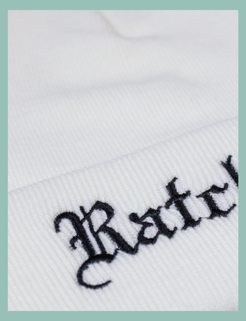 Close-up shot of the embroidery on the Ratchet Beanie in White by KULT Clothing | Black embroidered "Ratchet" in old English blackletter style on a white acrylic knitted beanie